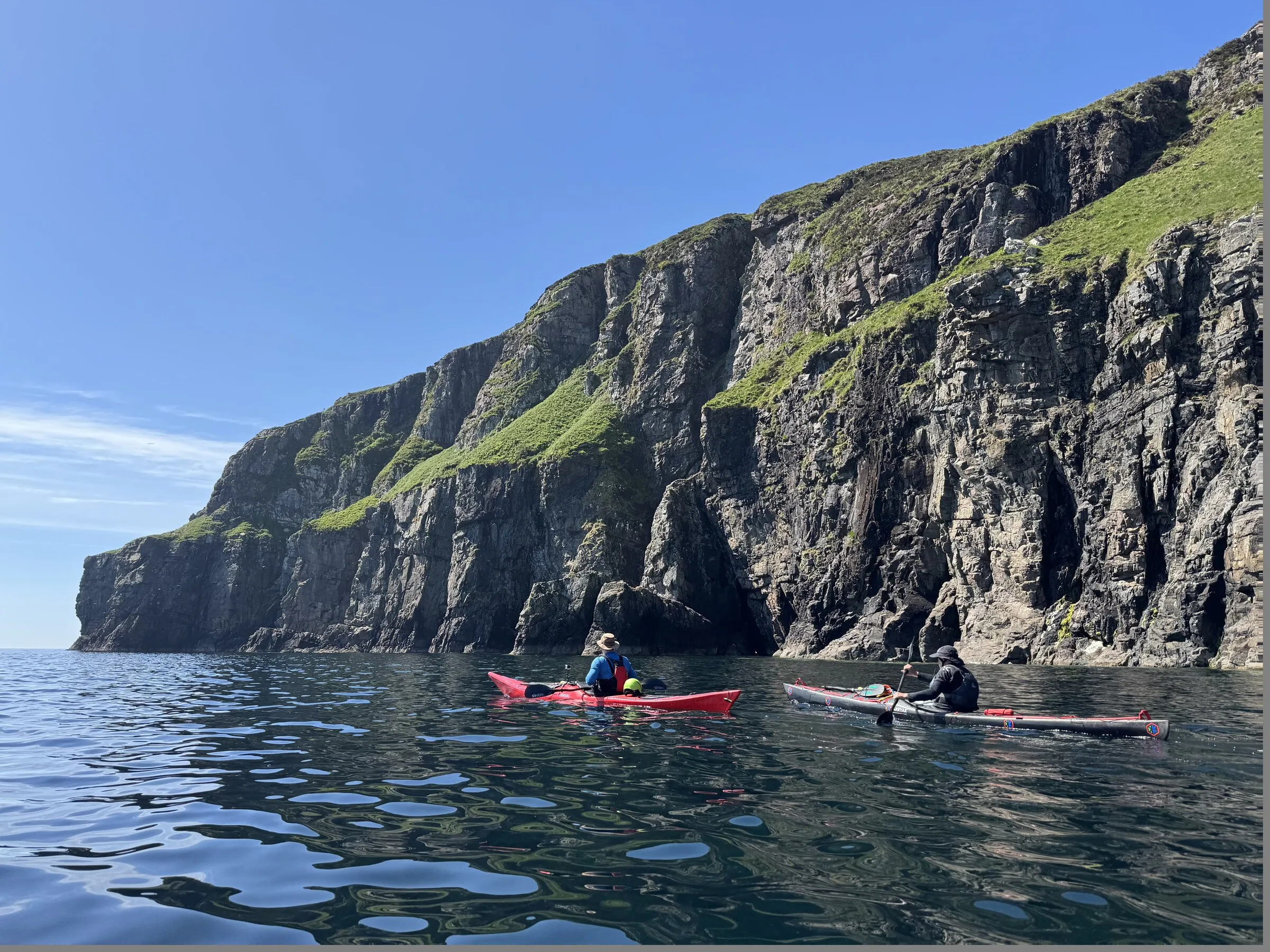 Two sea kayakers below high coastal cliffs in the Scottish Small Isles